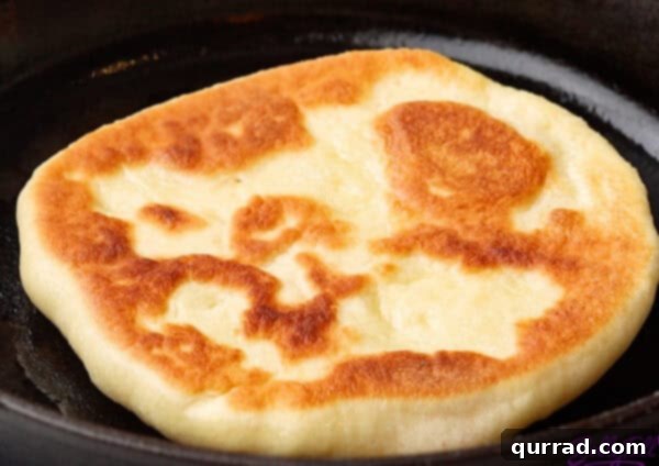 Pillowy Indian Flatbread 14 Golden-brown naan bread cooking in a cast iron skillet after being flipped, showing blisters