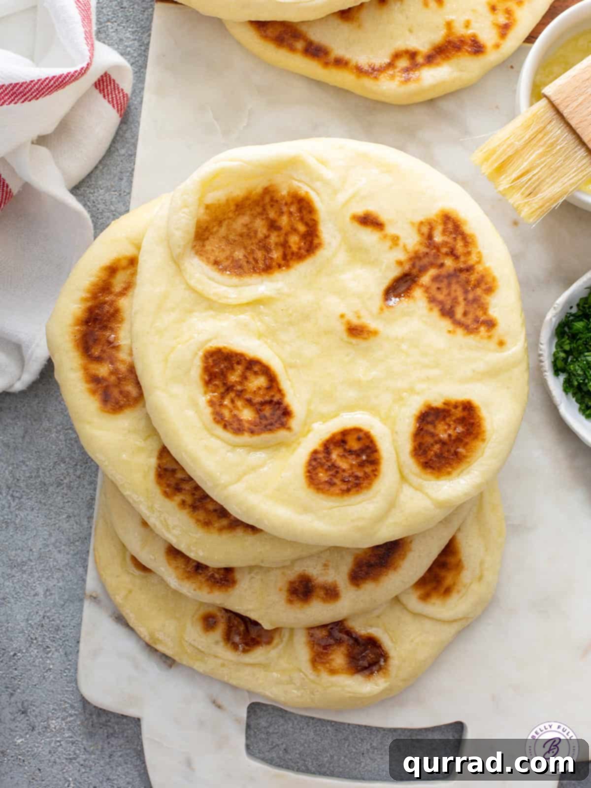 Stack of Perfectly Cooked Homemade Naan Stack of four warm, golden-brown naan flatbreads on a wooden cutting board