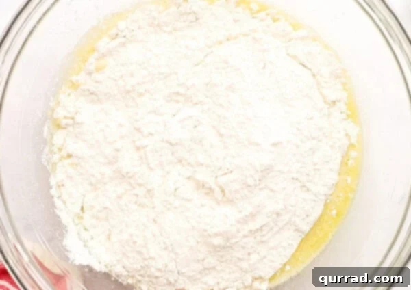Pillowy Indian Flatbread 4 All-purpose flour being added on top of the wet ingredients in a glass bowl