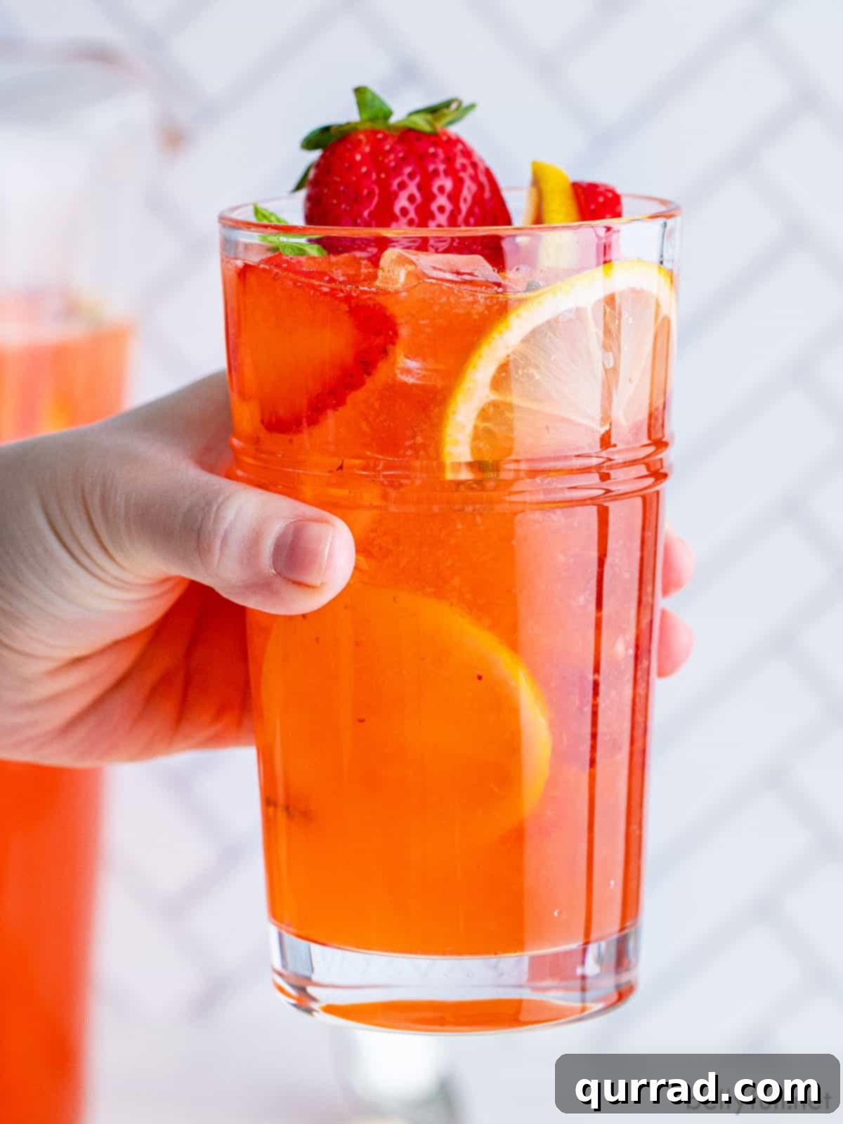 Vibrant Strawberry Lemonade 6 A hand gracefully holds a glass of freshly made strawberry lemonade, sparkling with ice and garnished with a lemon wedge and strawberry slice, inviting a cooling sip.