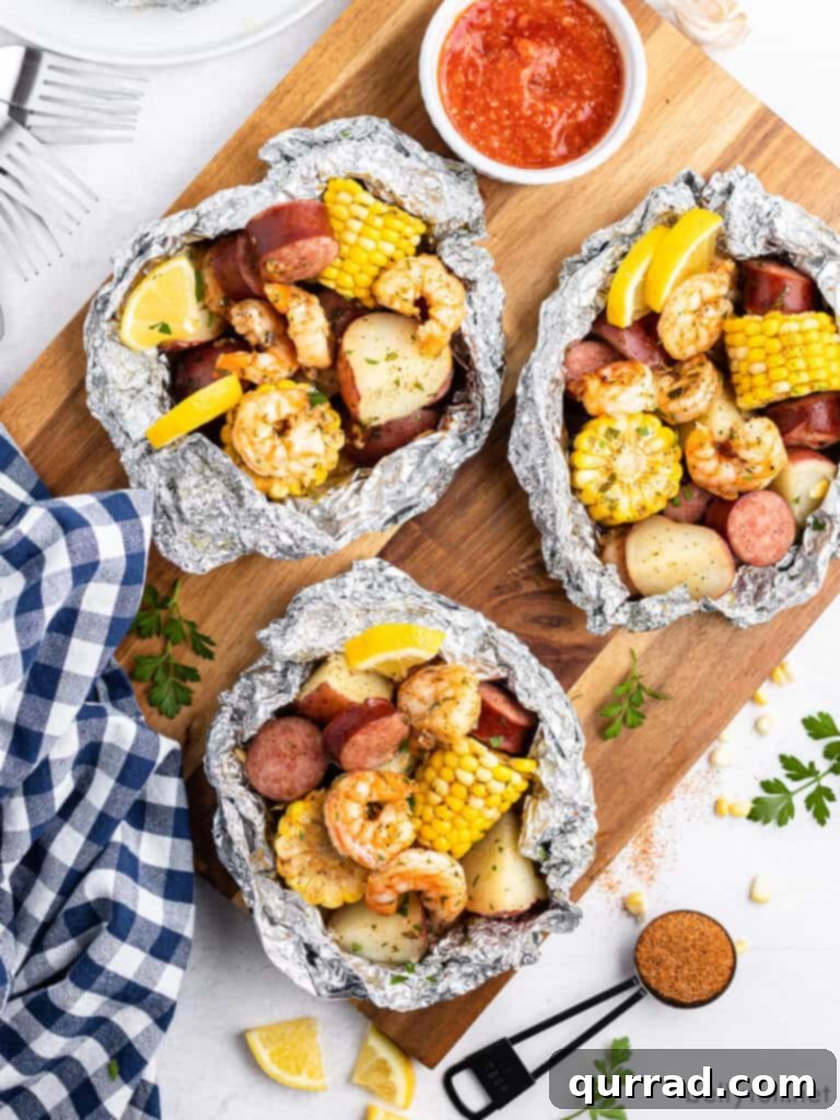 Garlic Butter Shrimp Boil Foil Packs 3 Overhead view of three perfectly sealed shrimp boil foil packets on a rustic cutting board, ready for cooking
