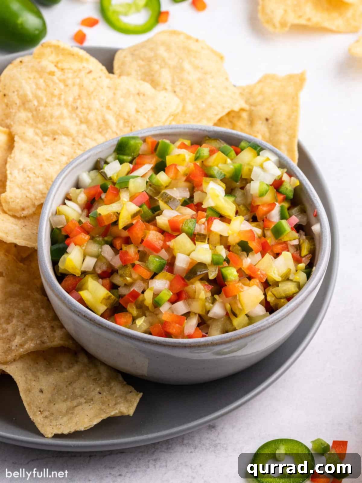Dill Pickle de Gallo 2 A bowl of vibrant green Pickle de Gallo surrounded by crispy golden tortilla chips, inviting a refreshing dip.