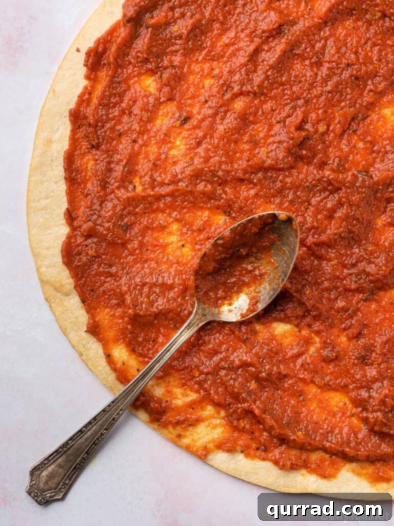 Overhead shot of a spoon covered in rich homemade pizza sauce on a bed of pizza dough.