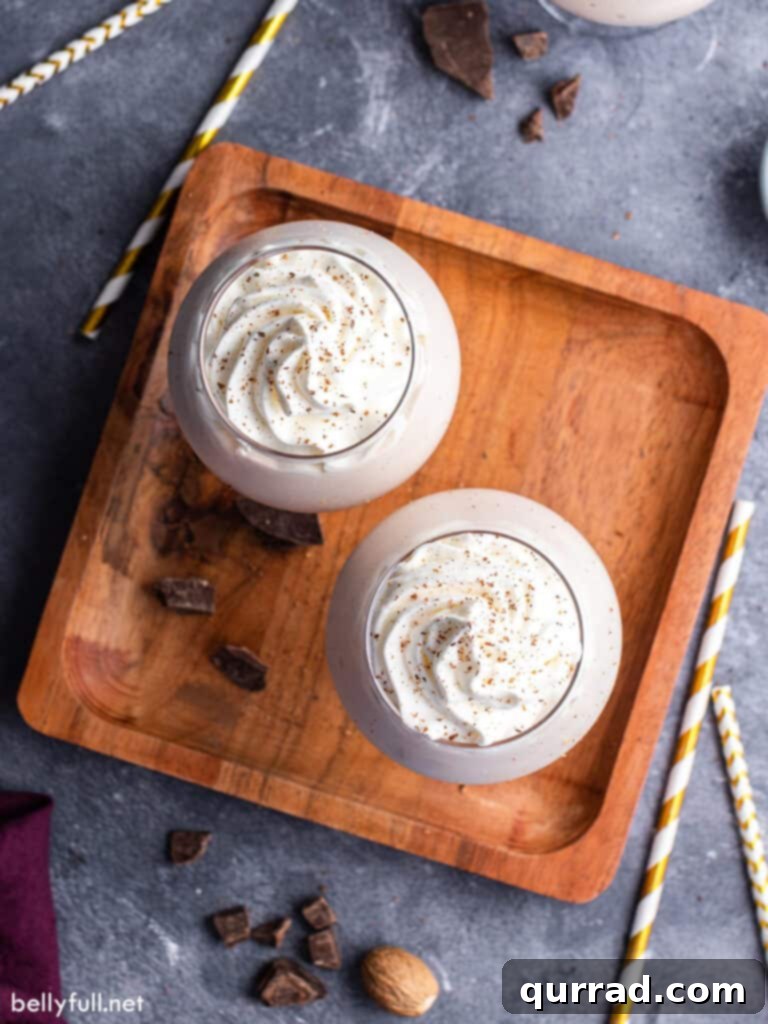Overhead view of two Brandy Alexander Milkshakes, generously topped with fluffy whipped cream and a dusting of fresh nutmeg.