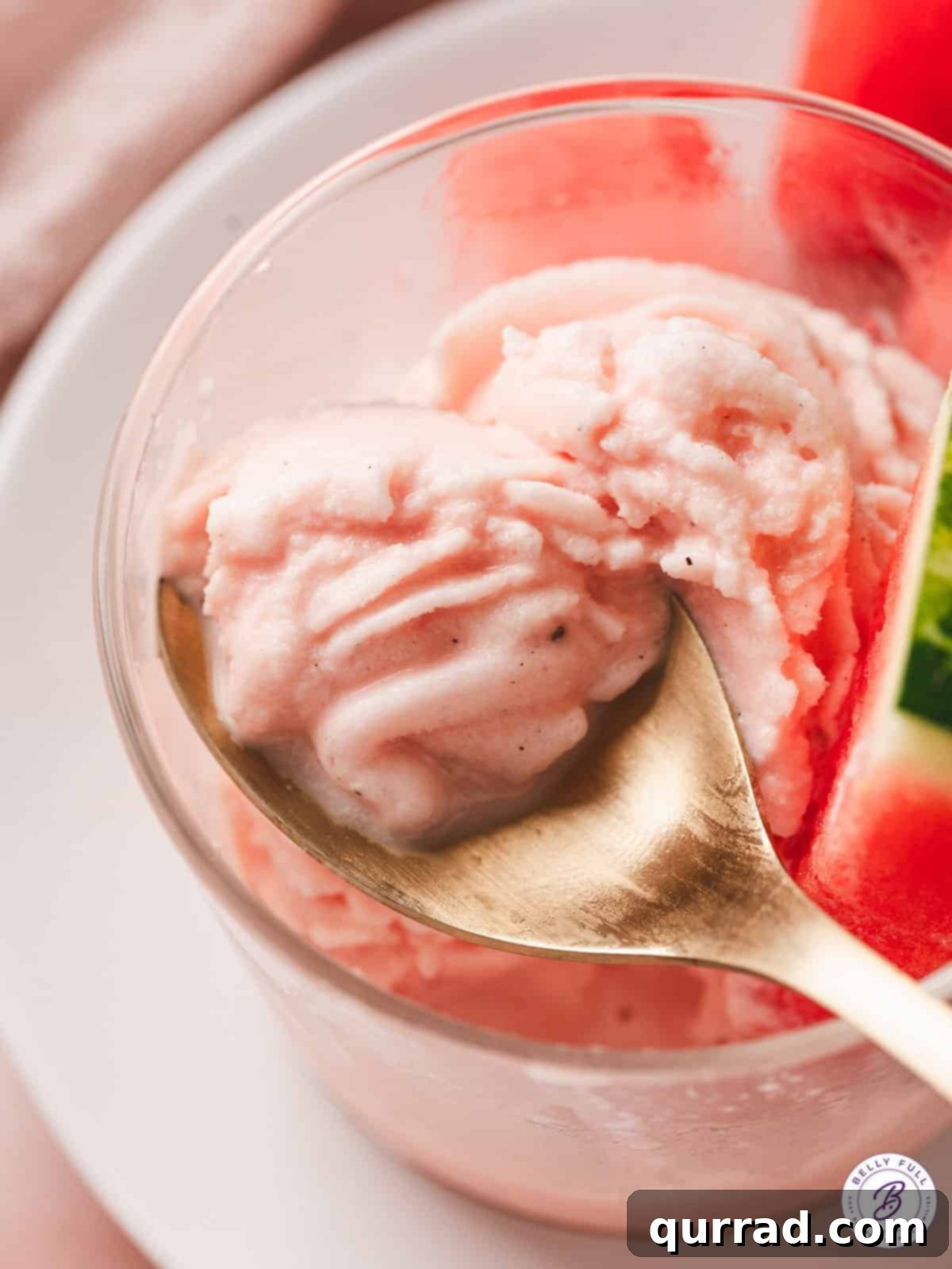 A spoon in a bowl of creamy pink watermelon dole whip, ready to be enjoyed.