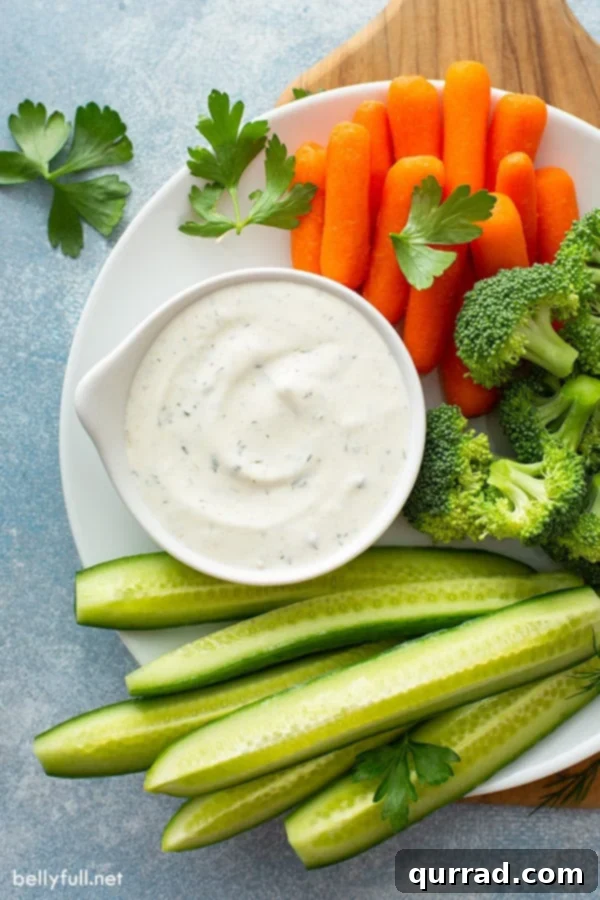 Aerial view of a plate featuring homemade ranch dip, surrounded by fresh cucumber slices, broccoli florets, and carrot sticks.