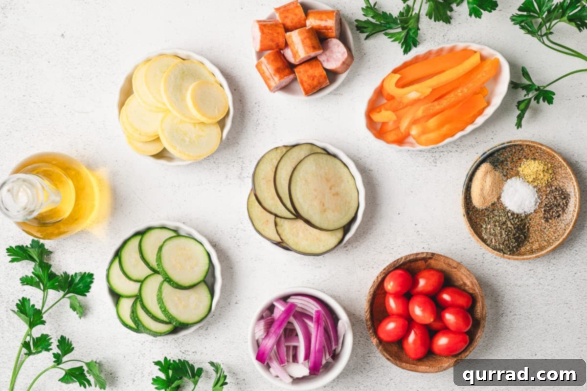Overhead view of ingredients needed to make sheet pan ratatouille including sliced vegetables, sausage, and spices