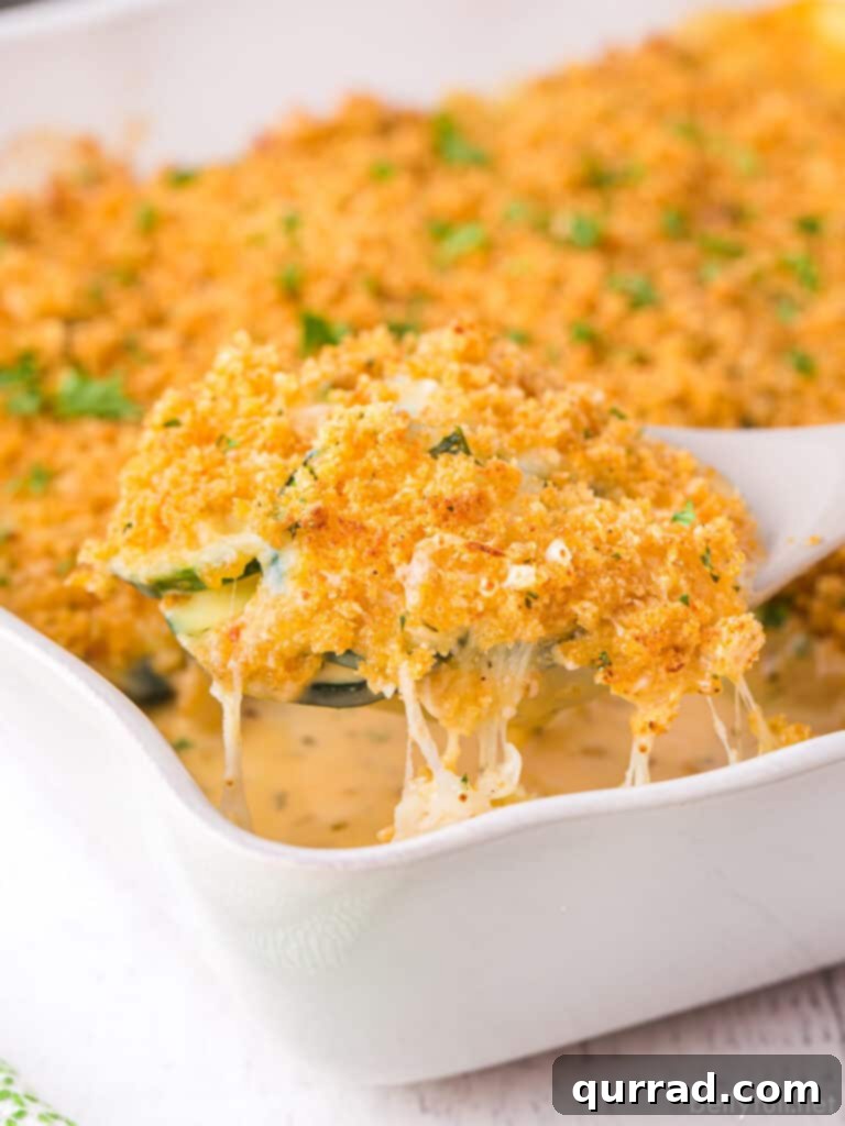 Perfect Cheesy Zucchini Bake 5 A white spoon lifting a serving of zucchini cheese casserole from the dish