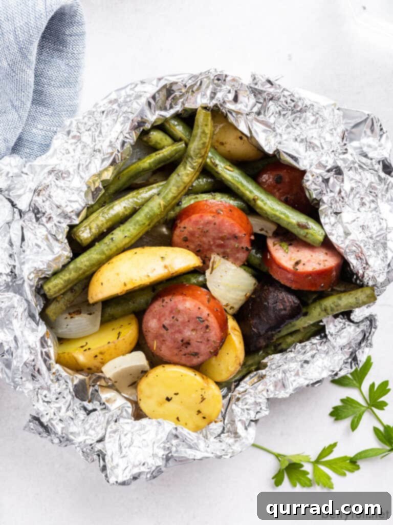 Savory Kielbasa & Veggie Bundles 2 Close-up of a perfectly cooked kielbasa and vegetable foil packet dinner, showcasing tender sausage slices, vibrant green beans, and roasted potatoes.