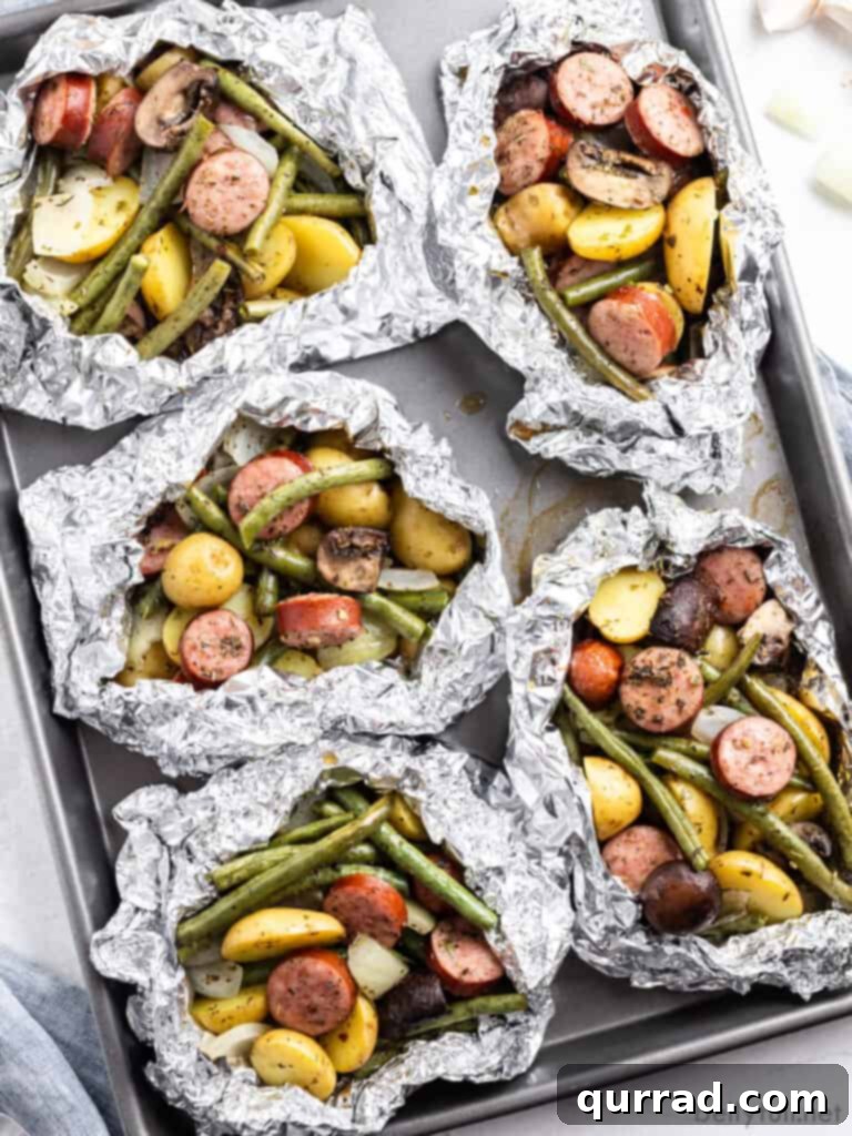 Savory Kielbasa & Veggie Bundles 3 Overhead view of five perfectly cooked kielbasa and vegetable foil packets arranged on a baking sheet, ready to be served.