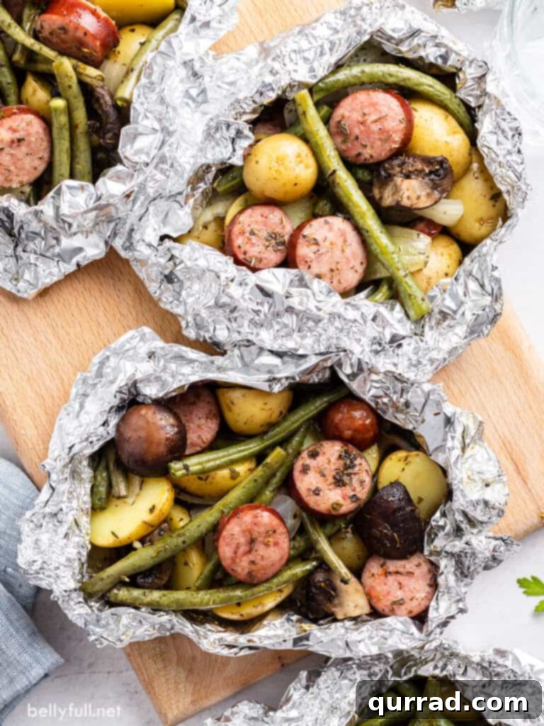 Savory Kielbasa & Veggie Bundles 4 Overhead view of cooked sausage and vegetable foil packets, freshly opened and arranged on a wooden cutting board, revealing steaming hot, colorful contents.