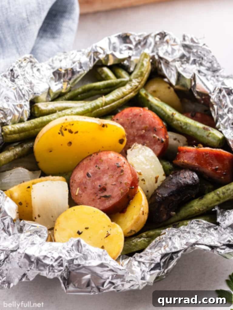 Savory Kielbasa & Veggie Bundles 5 Close-up of a single, perfectly opened kielbasa and vegetable foil packet, revealing steam rising from the flavorful meal inside.