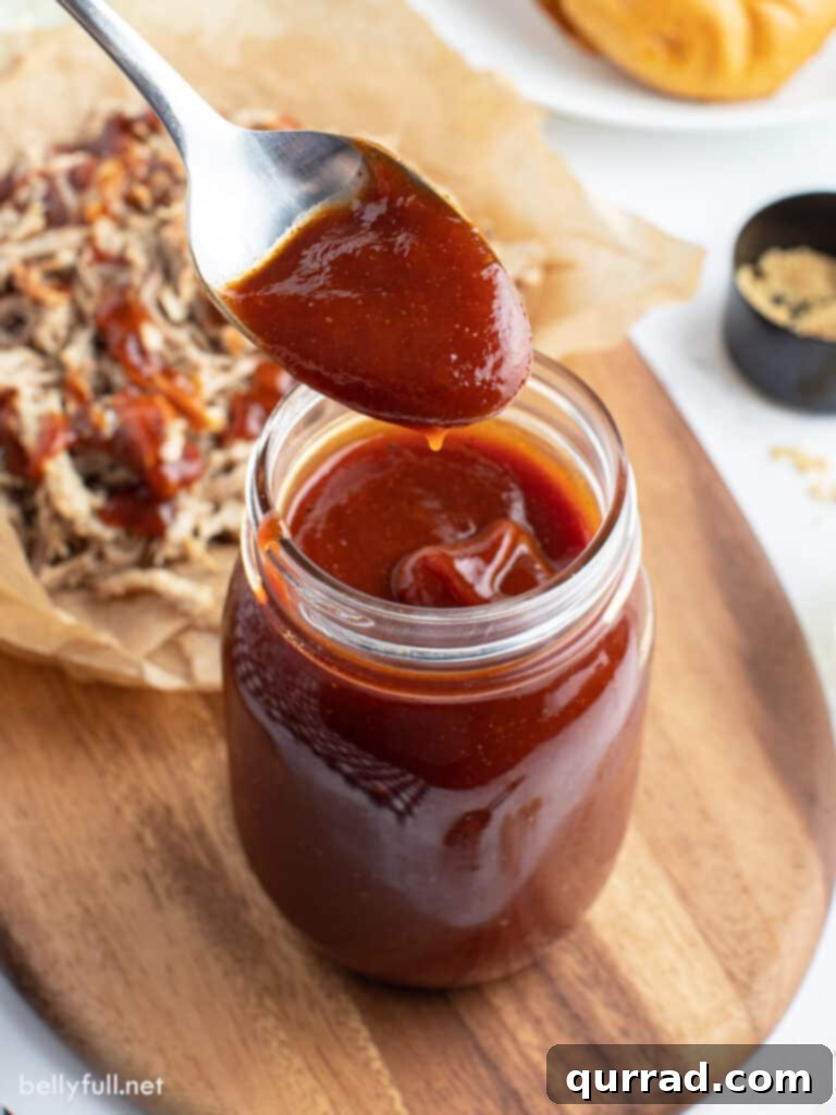 Grill Master's Secret BBQ Sauce 2 A spoonful of rich, homemade BBQ sauce being lifted from a glass jar, showcasing its thick, glossy texture and inviting deep reddish-brown color.