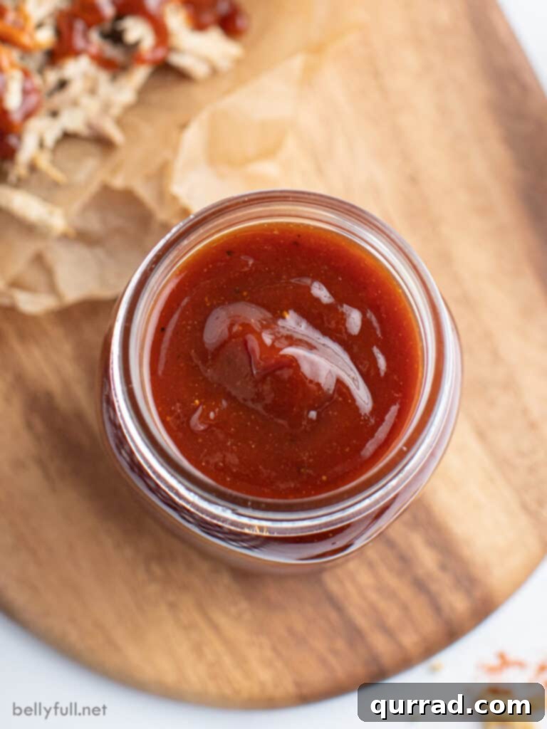 Grill Master's Secret BBQ Sauce 3 An inviting overhead shot of homemade BBQ sauce in a clear glass jar, with a wooden spoon resting beside it, highlighting its rich texture and color.