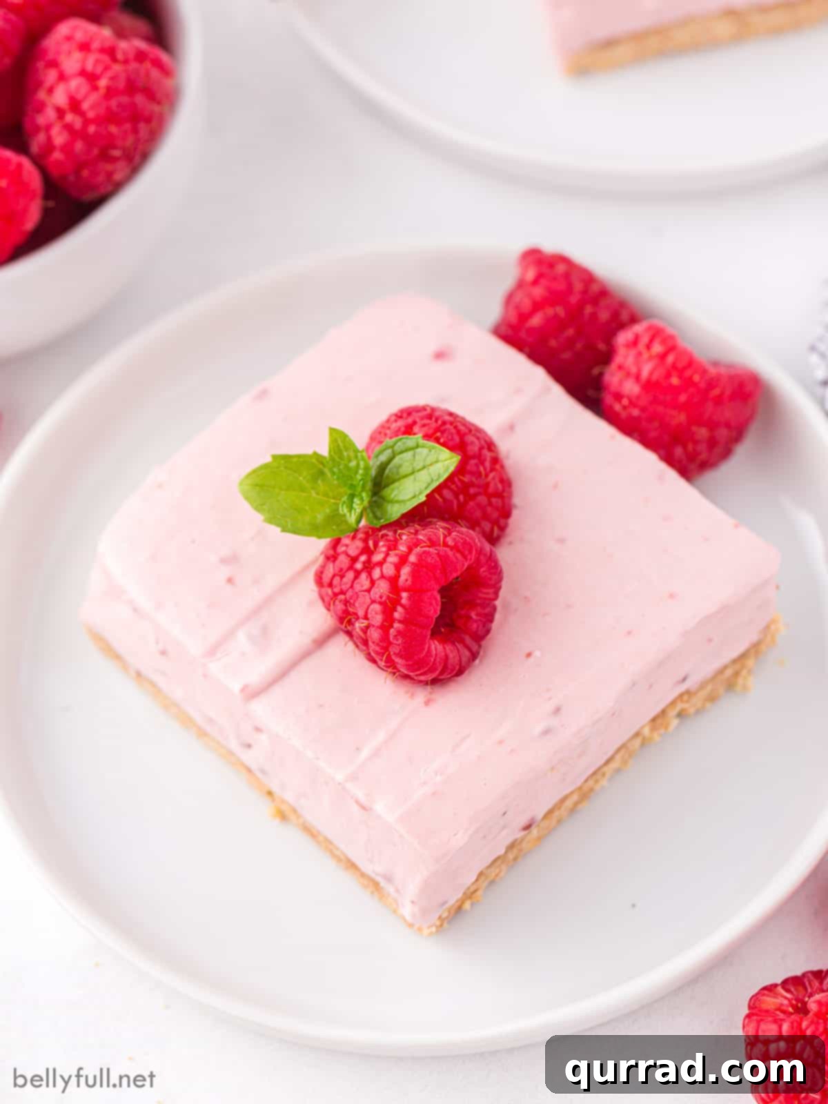 A raspberry bar topped with fresh raspberries on a white plate
