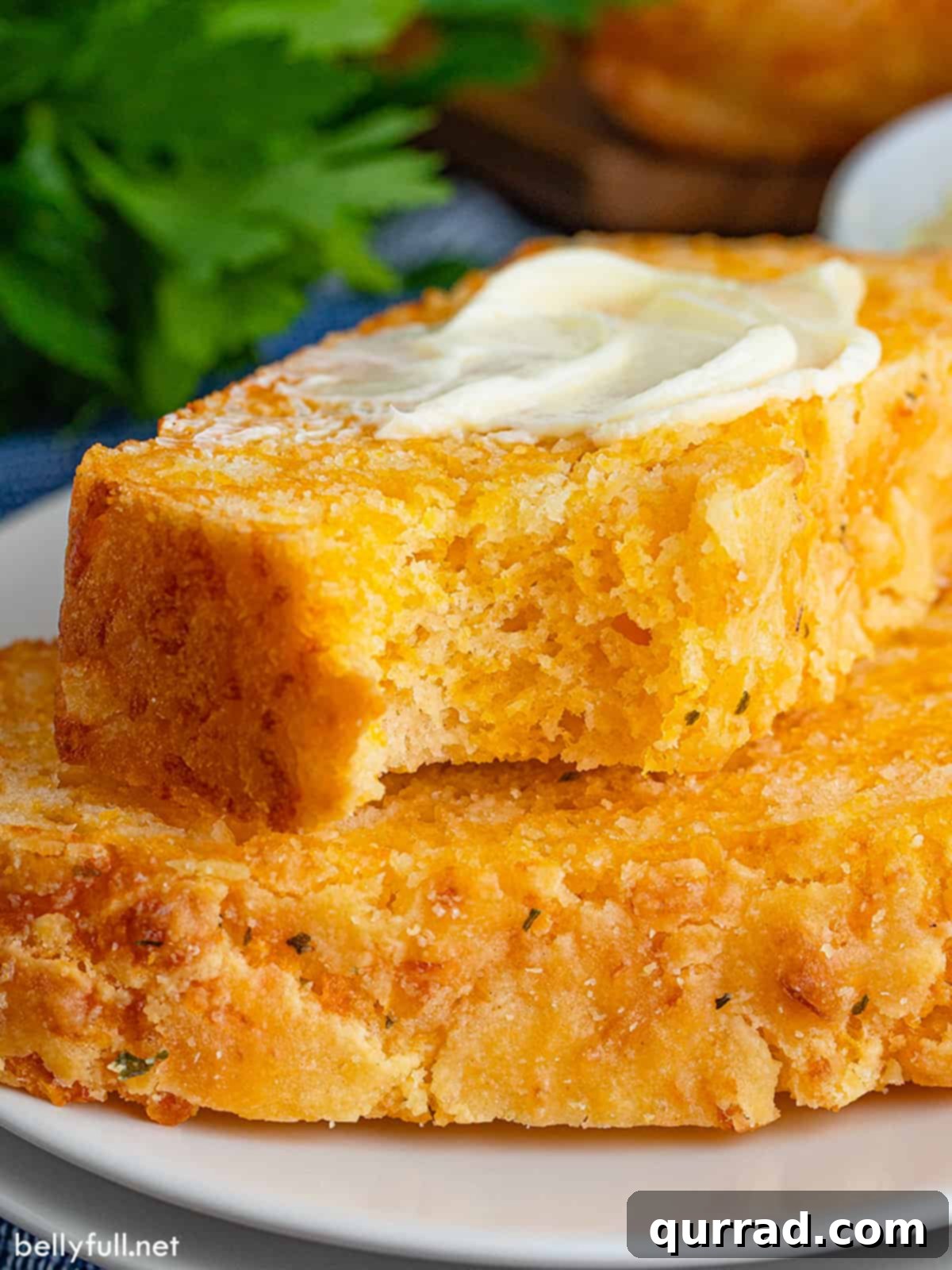 Cheesy Bread 4 Two slices of cheese bread, the top slice with a bite missing and butter spread on top, resting on a wooden board.