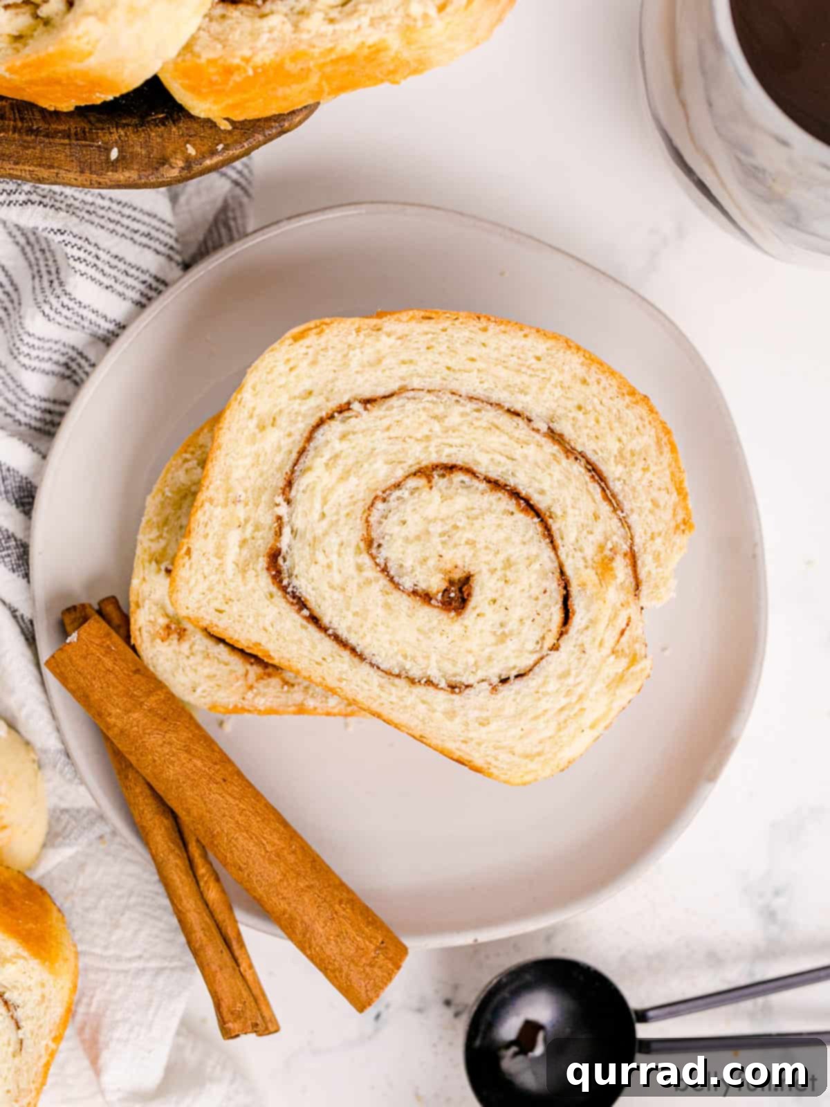 Sweet Cinnamon Swirl Loaf 2 Two slices of cinnamon swirl bread on a plate with a cinnamon stick, showcasing the beautiful swirl.