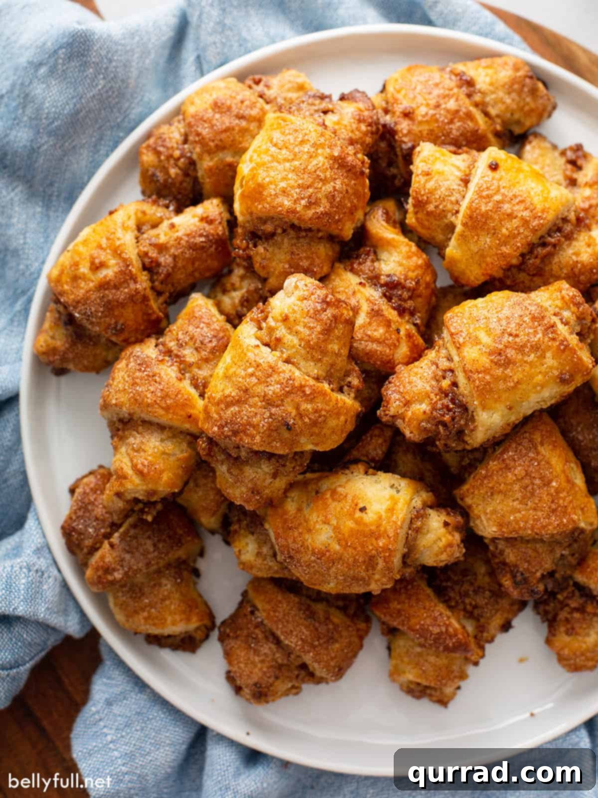 A white serving plate generously piled with perfectly baked Rugelach cookies, ready to be enjoyed.