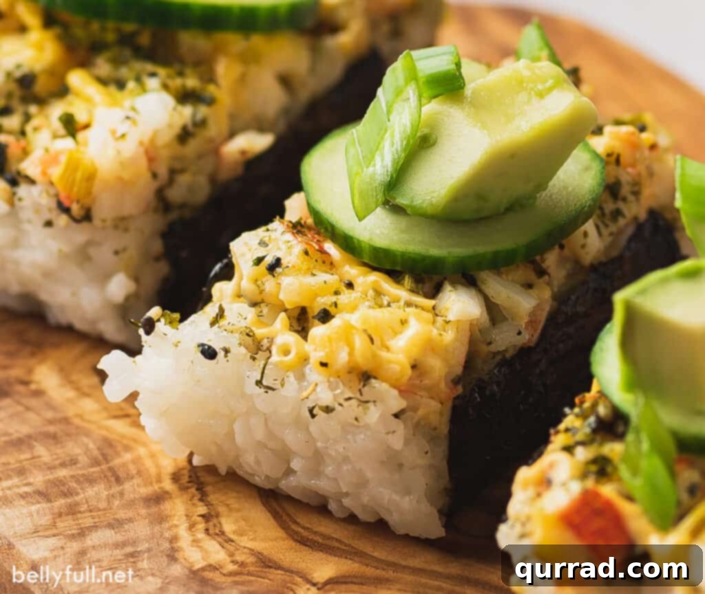 Baked Sushi Bliss 10 Close up of a portion of baked sushi casserole wrapped in nori and topped with cucumber, avocado and scallions.