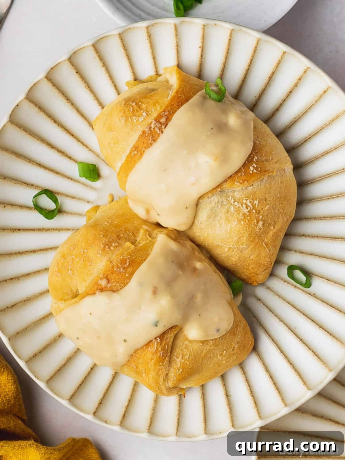 Two golden-brown chicken crescent roll ups, generously drizzled with creamy gravy and garnished with fresh herbs, showcasing their inviting texture.