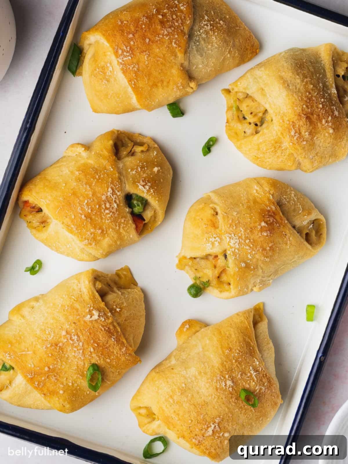 A baking sheet filled with perfectly golden-brown chicken crescent roll ups, each one slightly spaced apart, ready to be served.