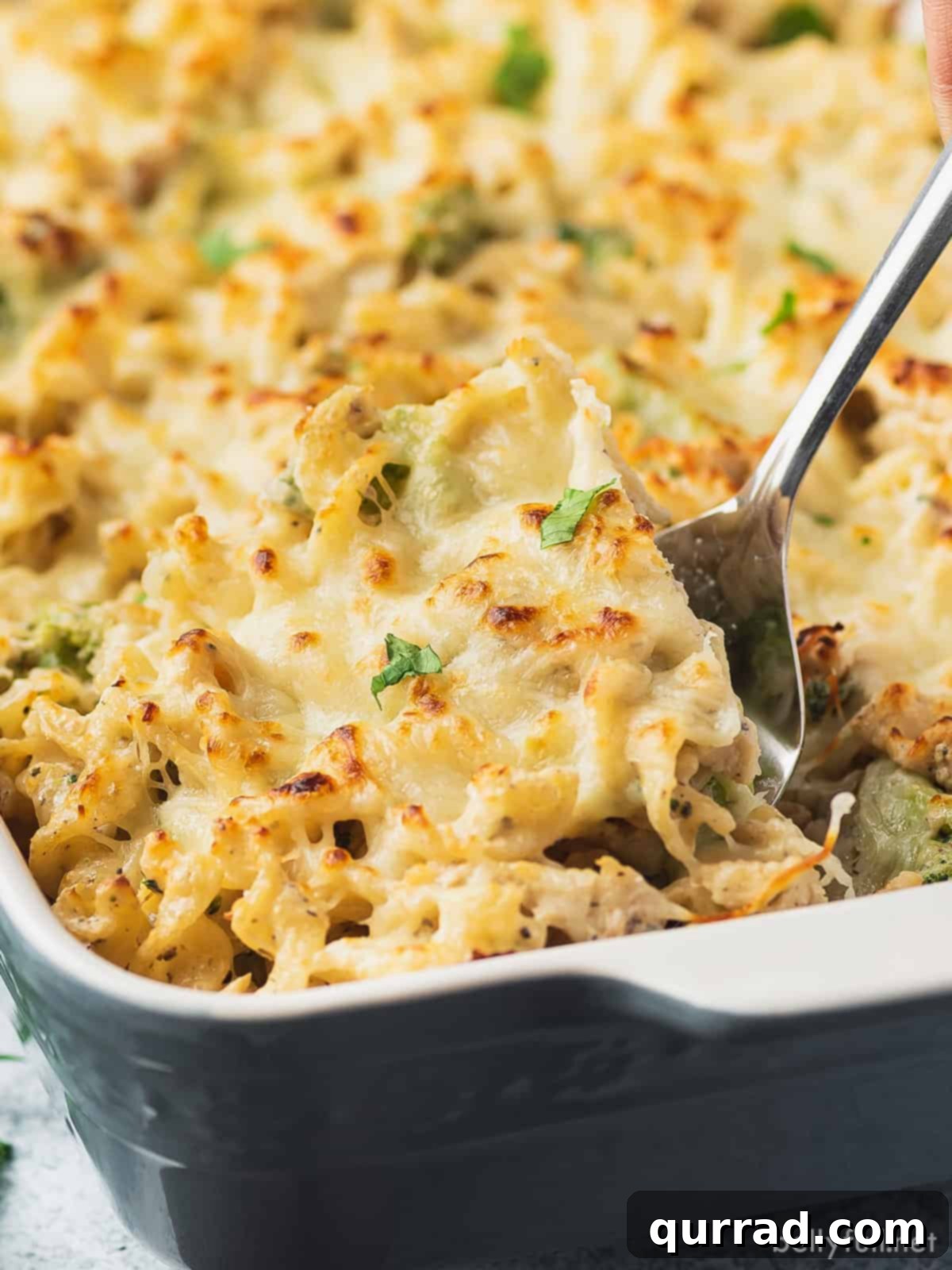 A silver spoon serving chicken alfredo bake, showing creamy sauce, chicken, pasta, and broccoli