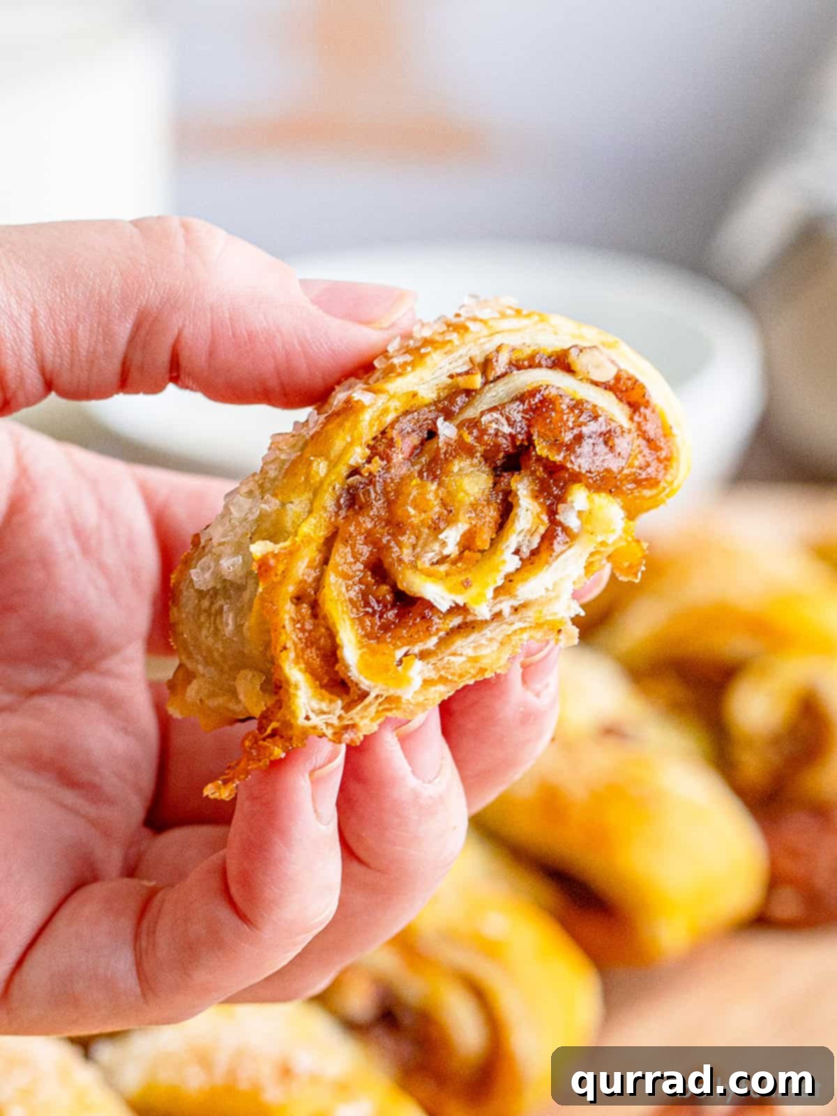 Cozy Pumpkin Pull-Apart Buns 2 A hand holding a piece of golden brown pumpkin pull-apart bread, showcasing its flaky layers and warm, spiced pumpkin filling, ready to be enjoyed.