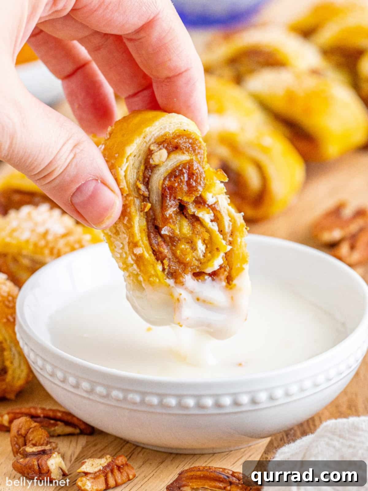 Cozy Pumpkin Pull-Apart Buns 5 A delicious piece of pumpkin pull-apart bread, revealing its layered pumpkin filling and flaky pastry, being dipped into a creamy vanilla glaze, highlighting the tempting texture and flavor.