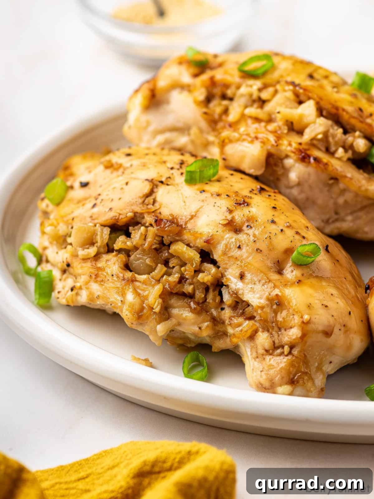 Fragrant Asian Rice Stuffed Chicken 2 Two golden-brown Asian rice stuffed chicken breasts on a white plate, garnished with fresh scallions, ready to be served.