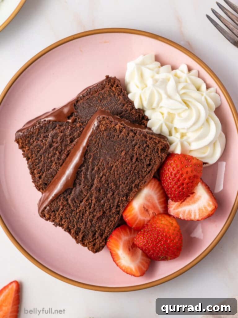 Two slices of glazed chocolate pound cake on a pink plate, garnished with fresh strawberries and a dollop of whipped cream.