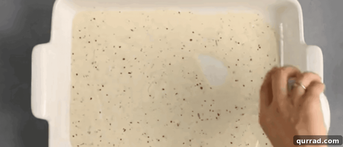 Alfredo sauce being poured into the bottom of the baking pan. 