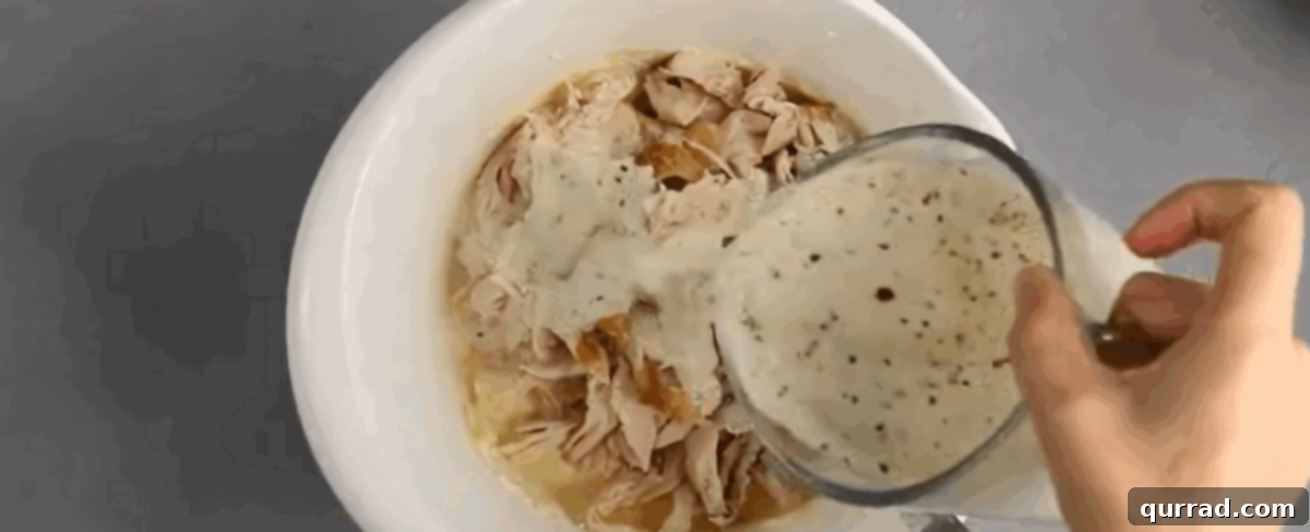 Combining the cheeses with the chicken and Alfredo sauce in a white bowl. 