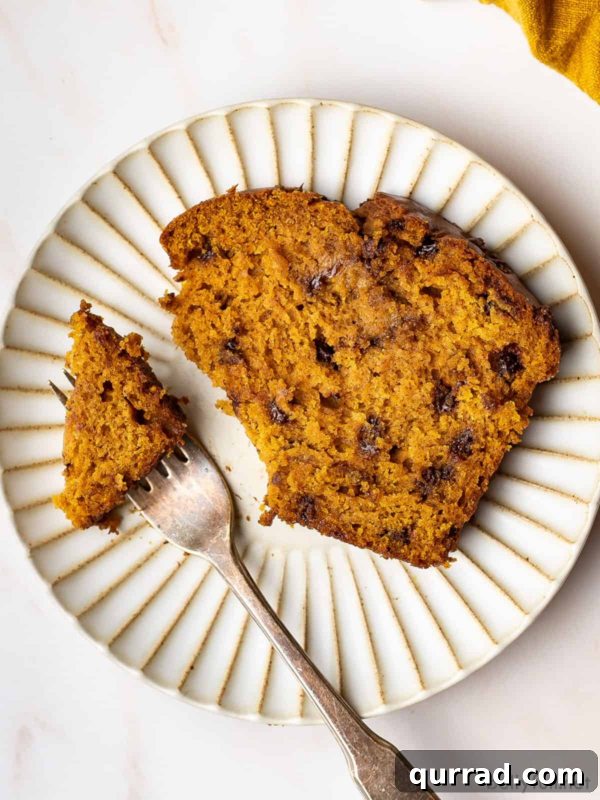 Harvest Pumpkin Chocolate Chip Loaf 4 A slice of chocolate chip pumpkin bread on a plate with a fork cutting off a bite, highlighting its soft texture and abundant chocolate chips.