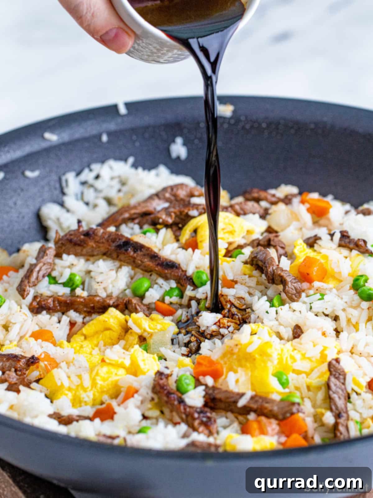 Savory Beef Fried Rice 5 Rich dark soy sauce being poured into a sizzling skillet with fried rice, enhancing its color and flavor.