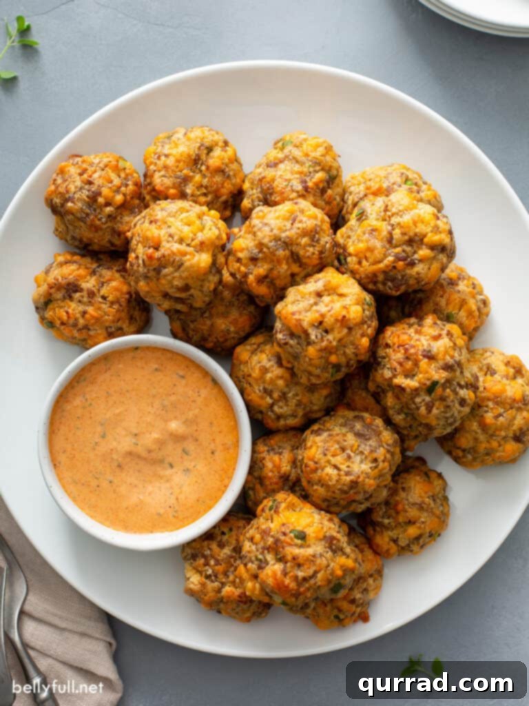Overhead shot of golden-brown sausage balls on a white plate, accompanied by a small bowl of creamy remoulade sauce, ready to be served at a gathering.