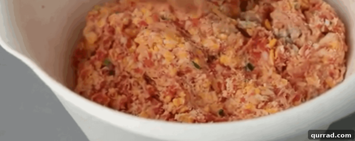 All the fresh ingredients for making sausage balls laid out in a white bowl, including ground pork, shredded cheddar cheese, biscuit mix, buttermilk, and scallions.
