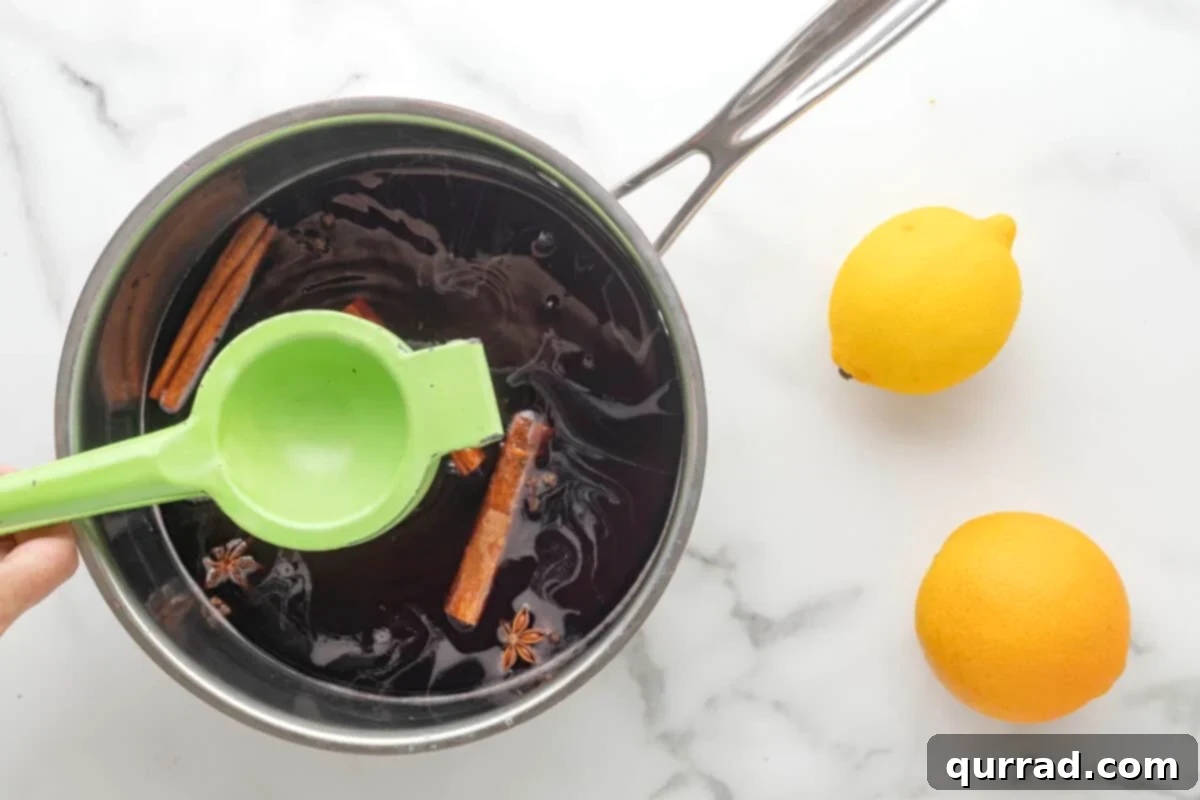 Spiced Winter Warmth 6 A hand squeezing lemon juice directly into the wine mixture in a pot, surrounded by orange slices and whole spices.