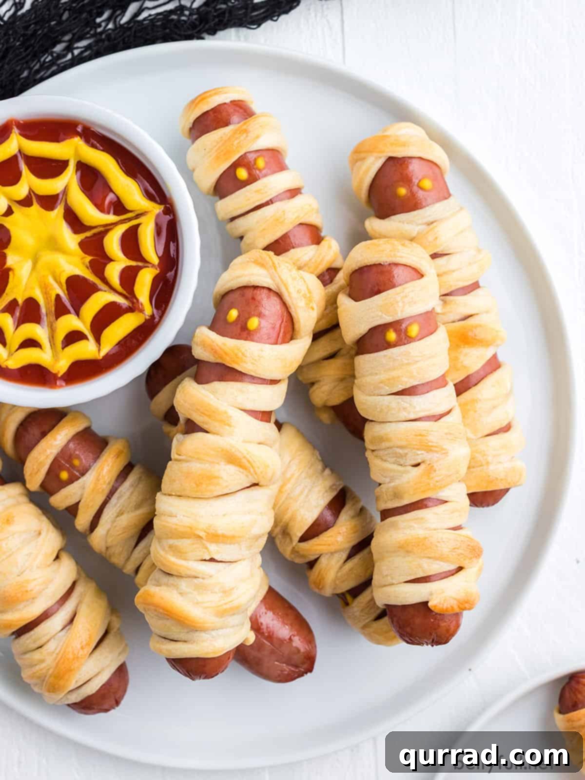 Frank-N-Mummies 2 Mummy dogs on a white plate with spiderweb sauce, ready for a Halloween party