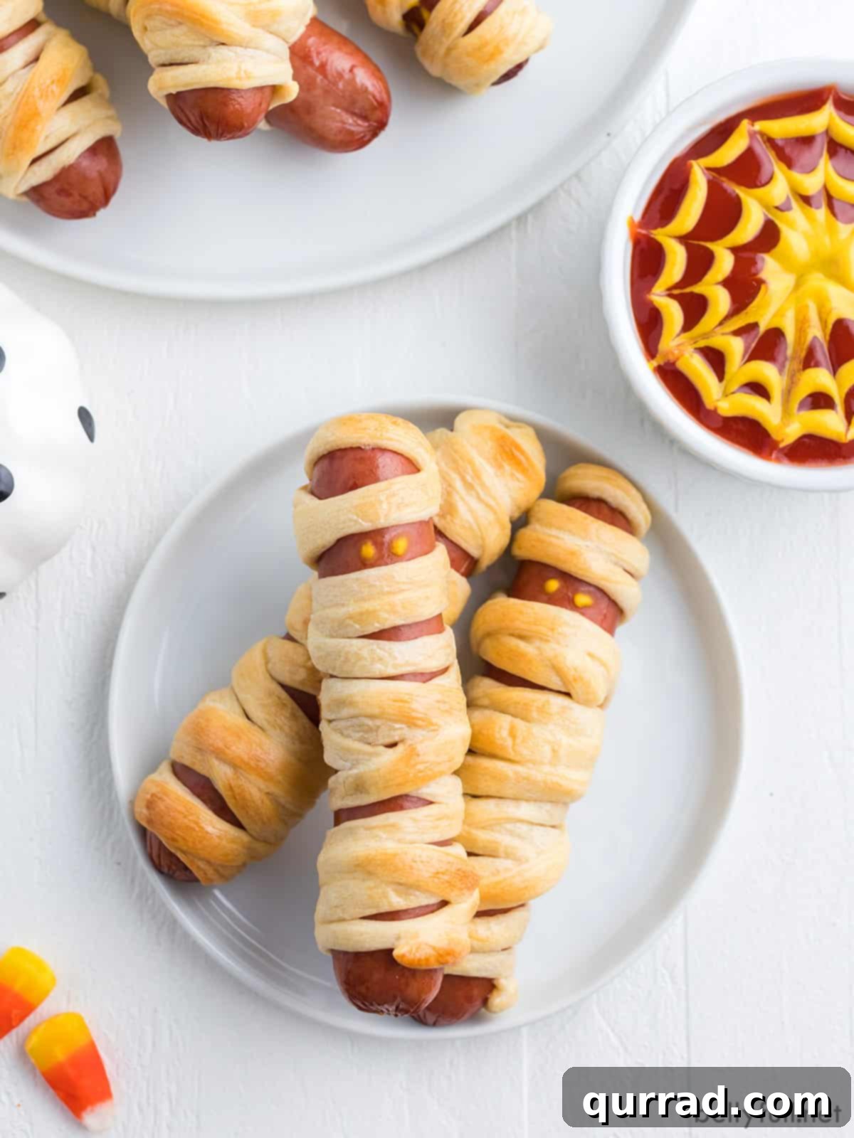 Frank-N-Mummies 3 Three golden brown mummy hot dogs displayed on a pristine white plate, showcasing their festive Halloween appeal