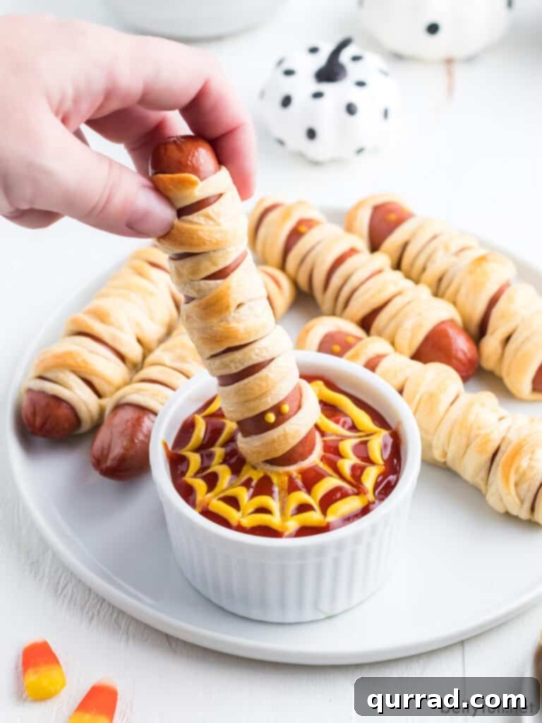 Frank-N-Mummies 4 A delicious mummy hot dog being dipped into a bowl of spooky spiderweb sauce