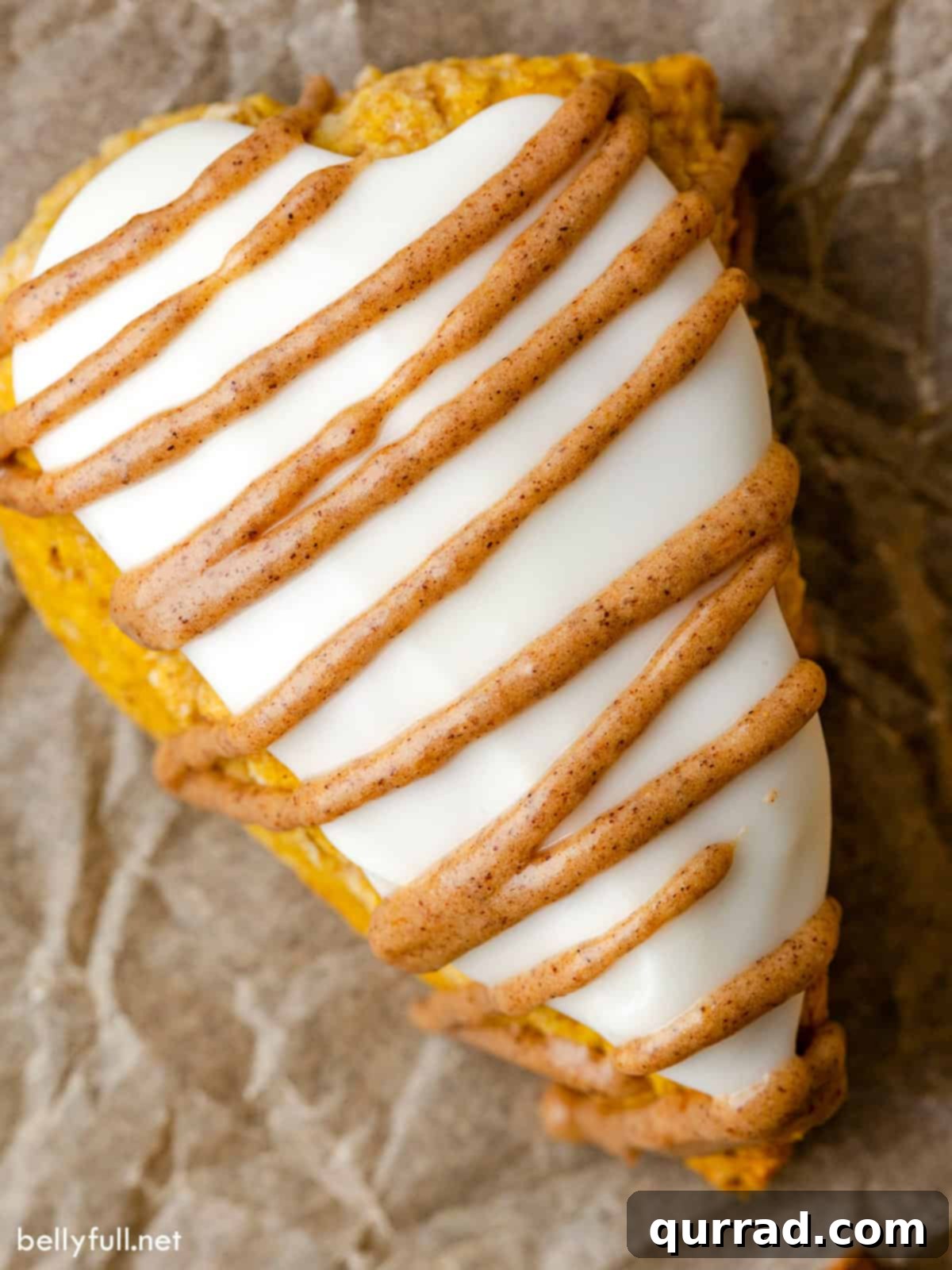 Close-up overhead view of a pumpkin scone with both vanilla and pumpkin glaze drizzled