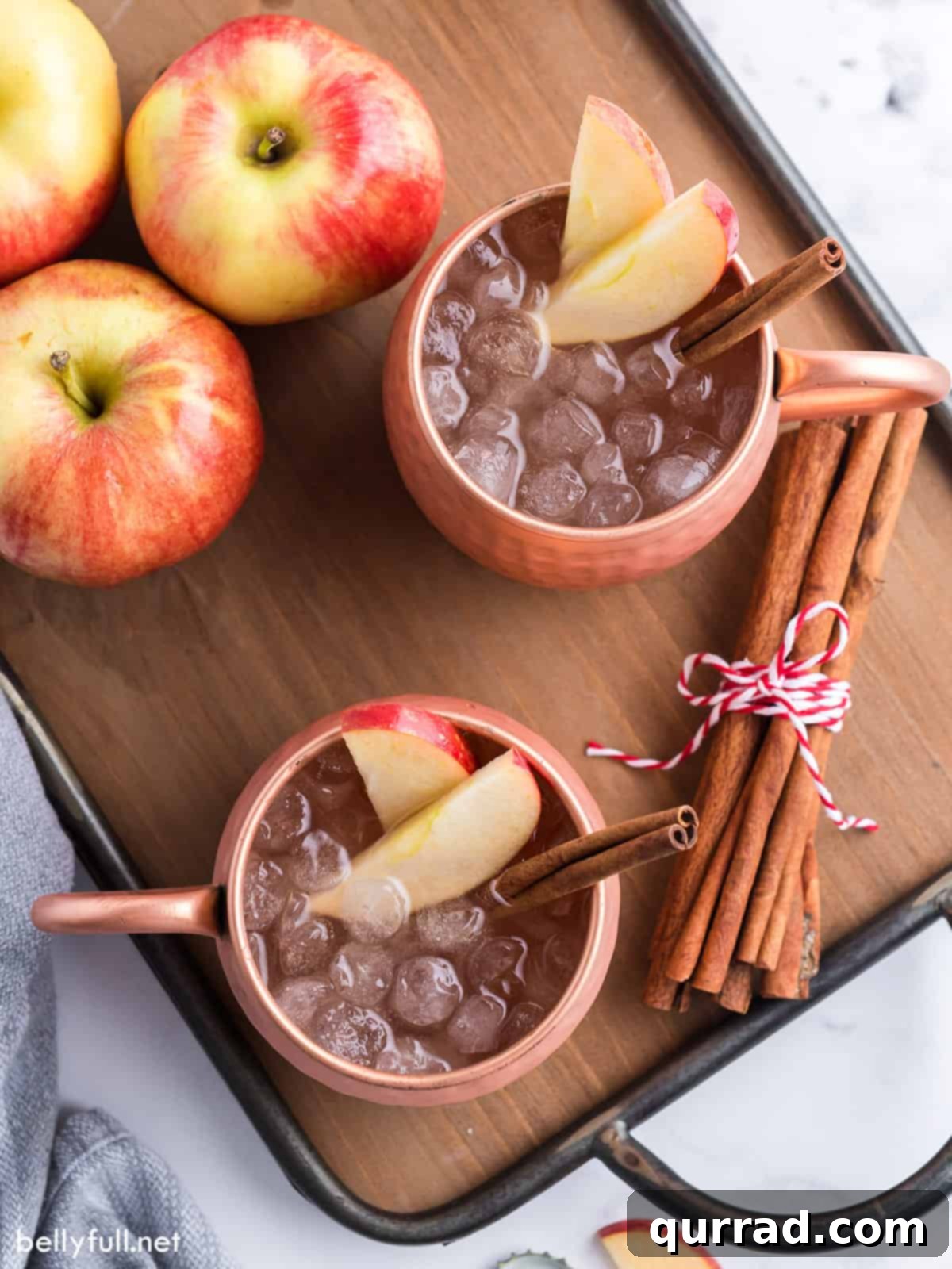 Crisp Apple Mule 4 An overhead shot showcasing two beautifully arranged Apple Cider Moscow Mules in copper mugs, adorned with fresh apple slices and cinnamon sticks.