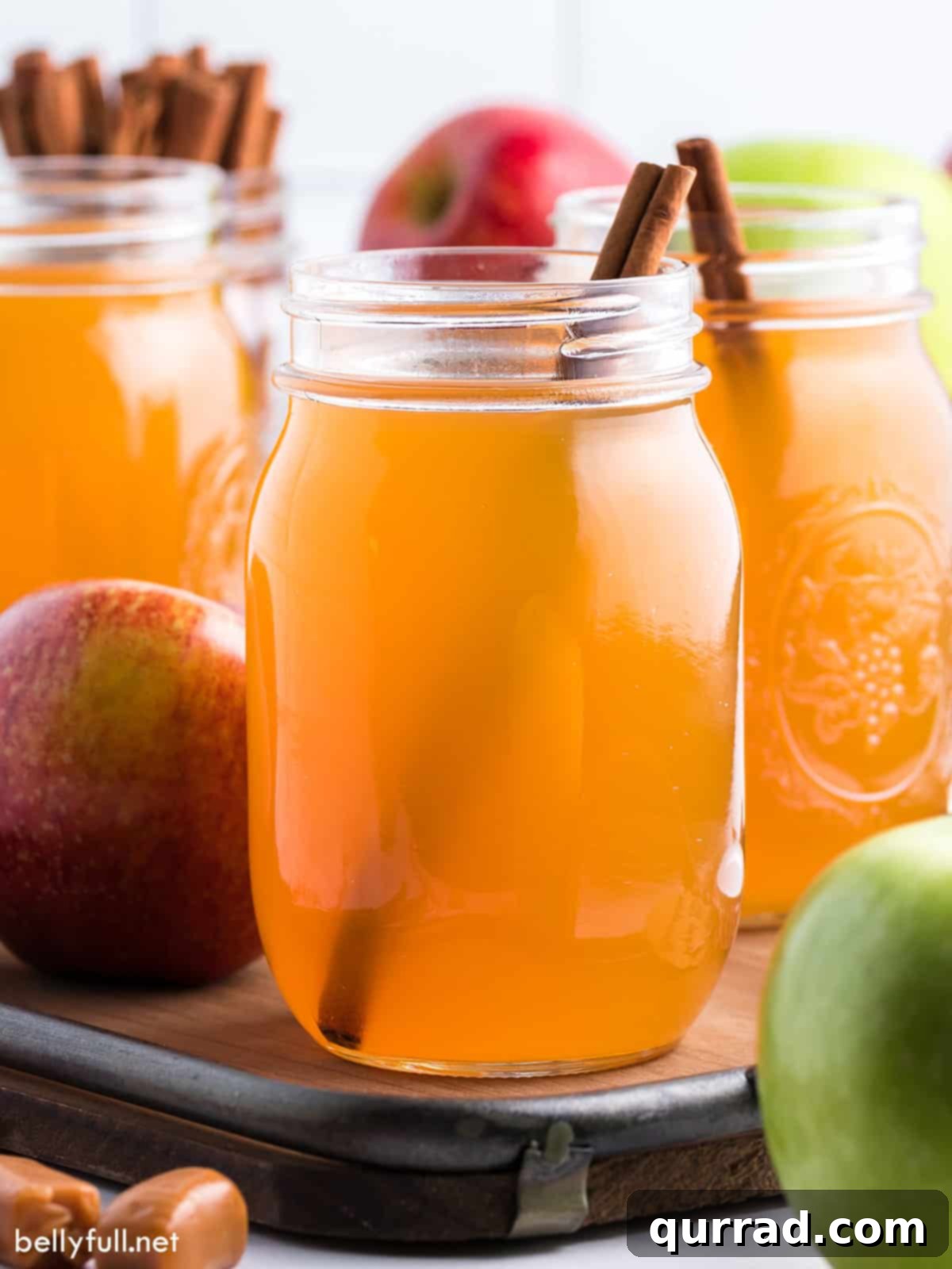 Mason jars of homemade apple pie moonshine garnished with a cinnamon stick
