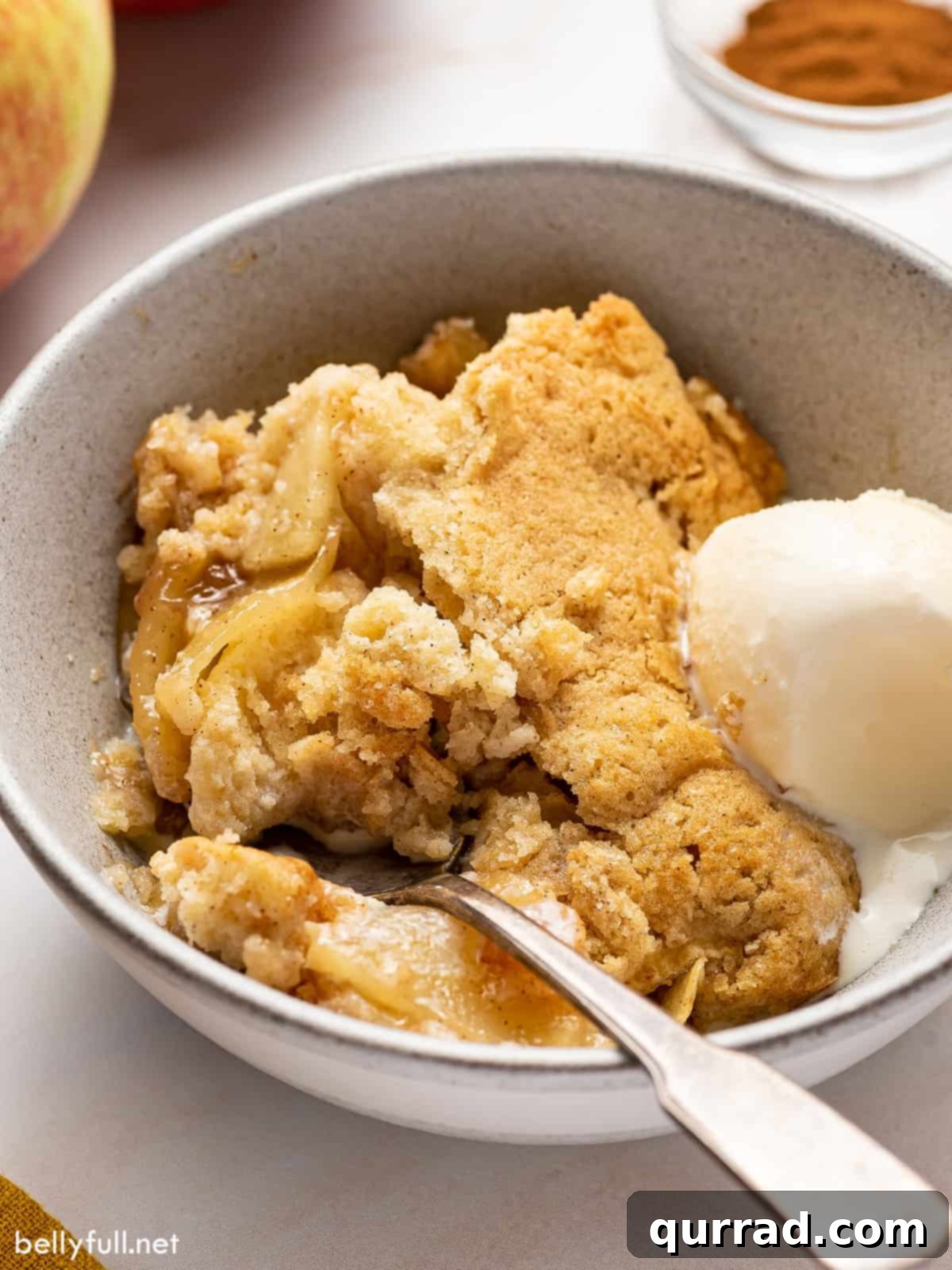 Sweet Cinnamon Apple Cobbler 2 A spoon digging into a bowl of warm apple cobbler with a melting scoop of vanilla ice cream