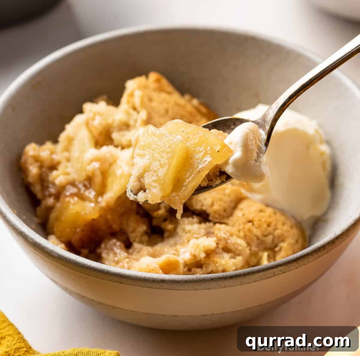 Sweet Cinnamon Apple Cobbler 5 Close-up of a spoon in a bowl of apple cobbler, showcasing the tender apples and biscuit topping