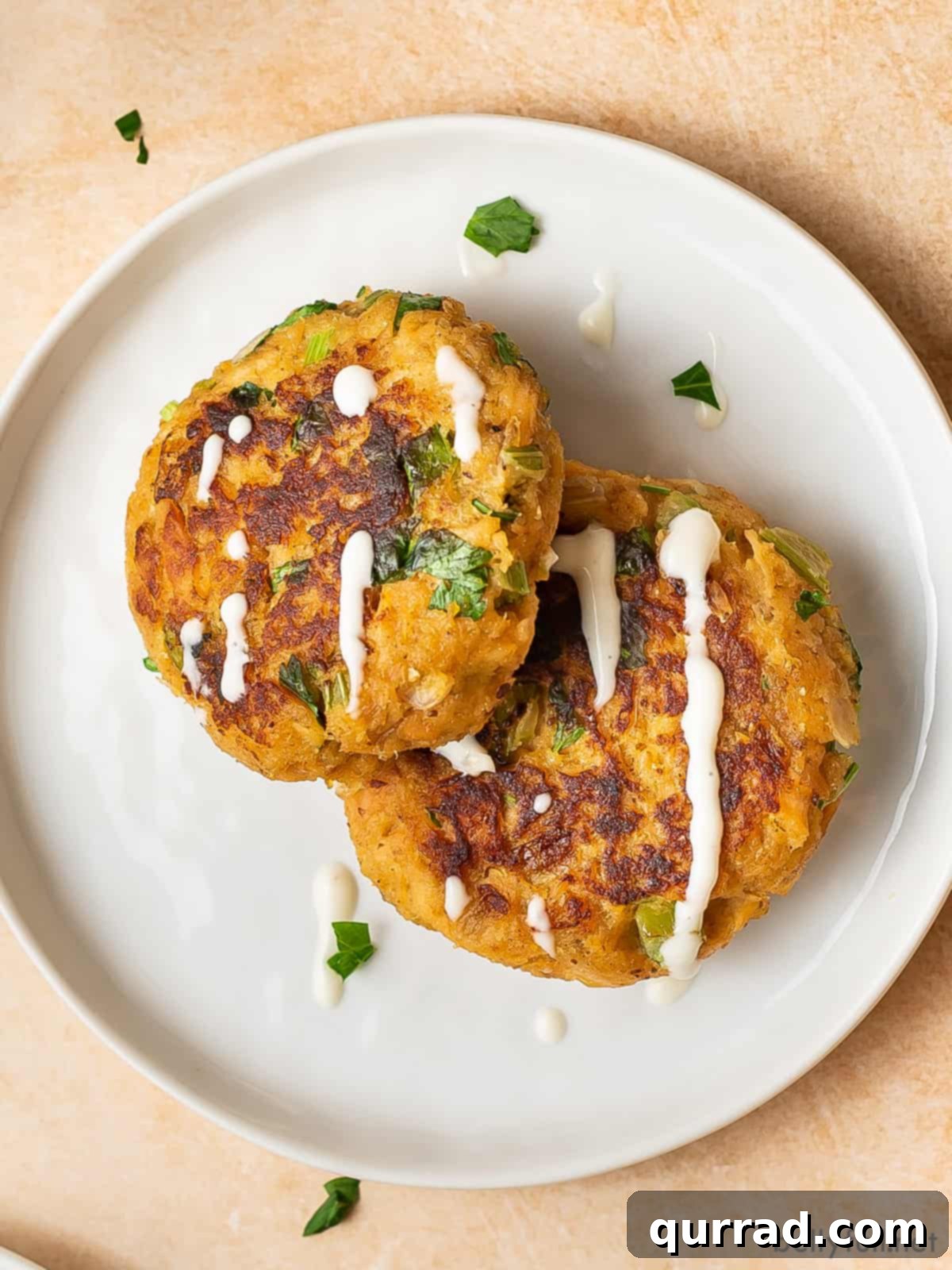 Savory Salmon Cakes 3 Two salmon cakes drizzled with tzatziki on a white plate
