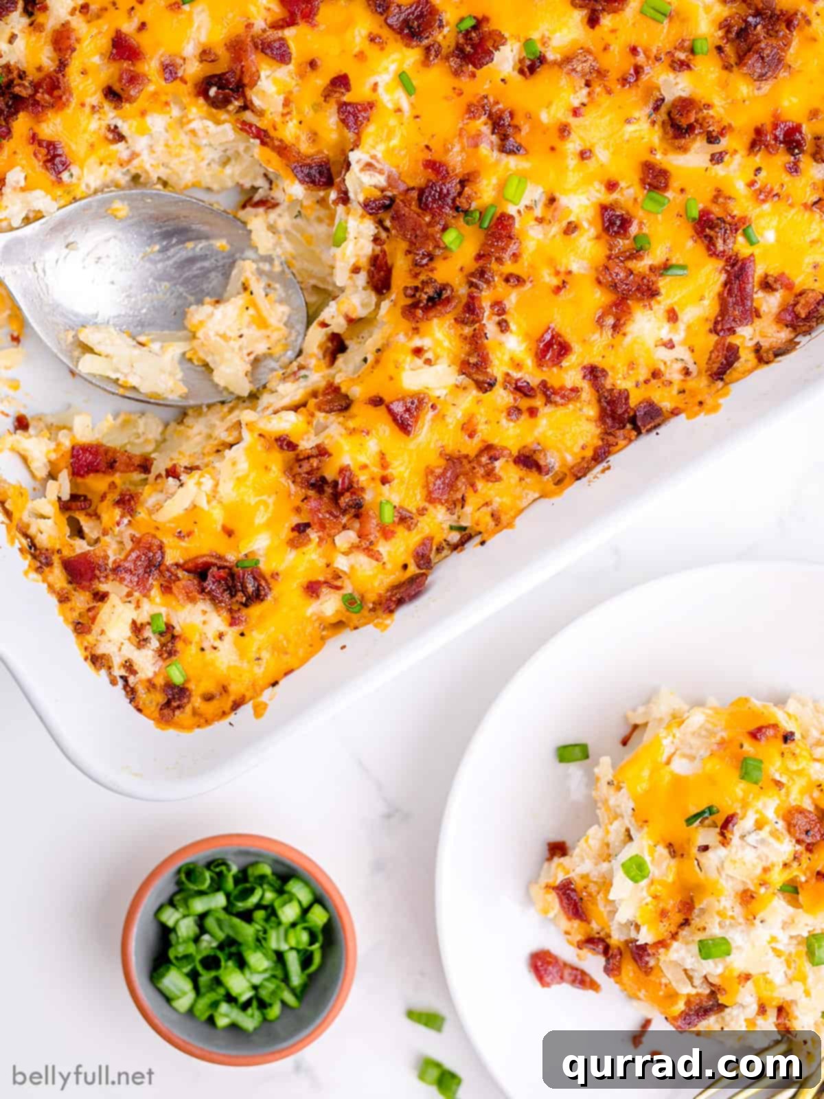 Golden Cheesy Potato Bake 2 A golden brown cheesy potatoes casserole with a serving on a white plate next to the baking dish, garnished with parsley.