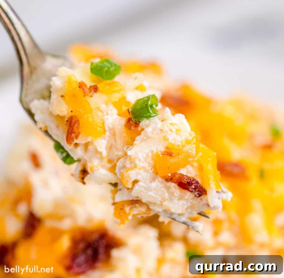 Golden Cheesy Potato Bake 4 A spoonful of hot, gooey cheesy hash brown potatoes being lifted from a casserole dish, showing melted cheese and bacon bits.