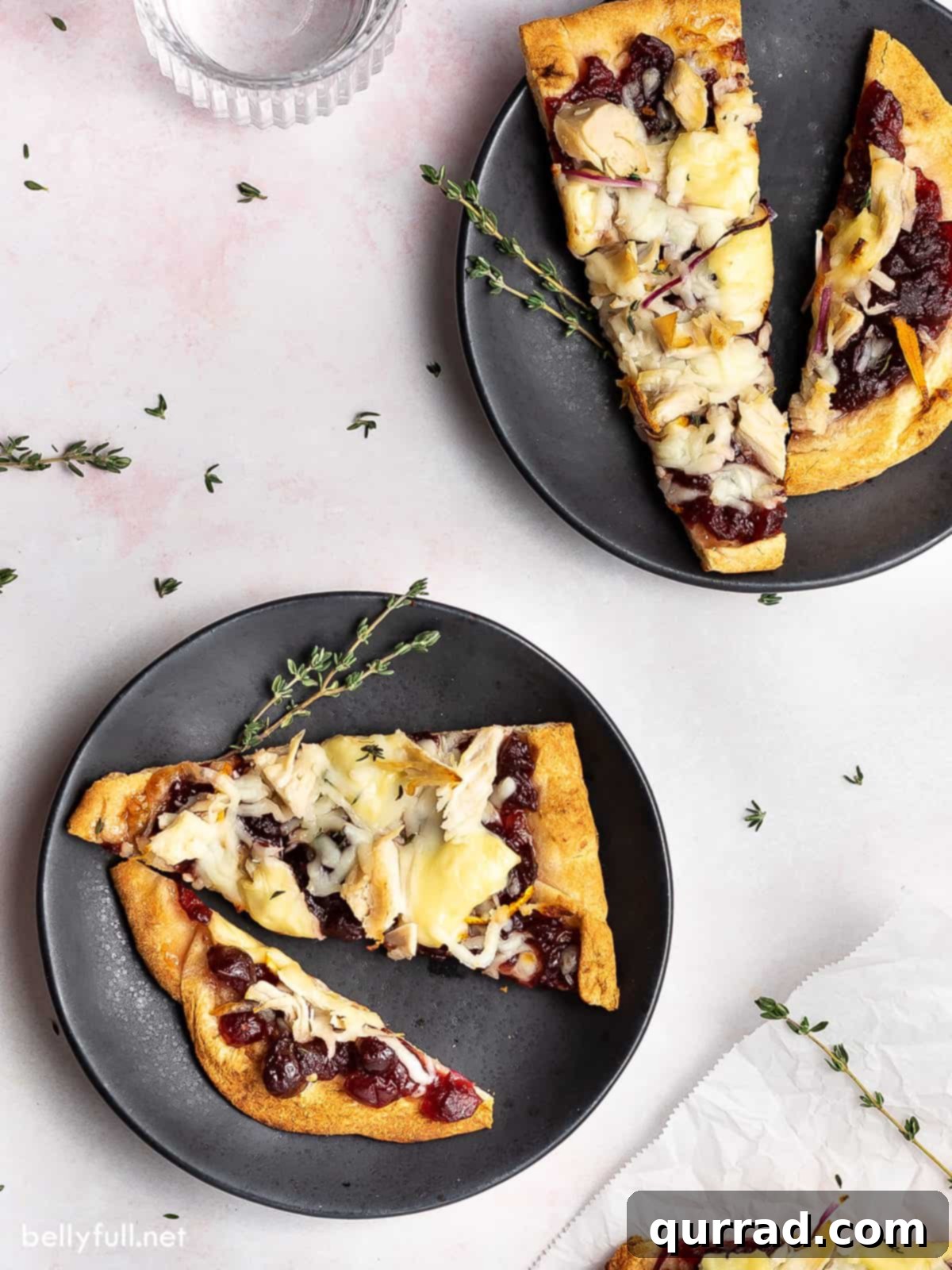 Two black plates with slices of Turkey Cranberry Brie Naan Pizza, garnished with fresh thyme