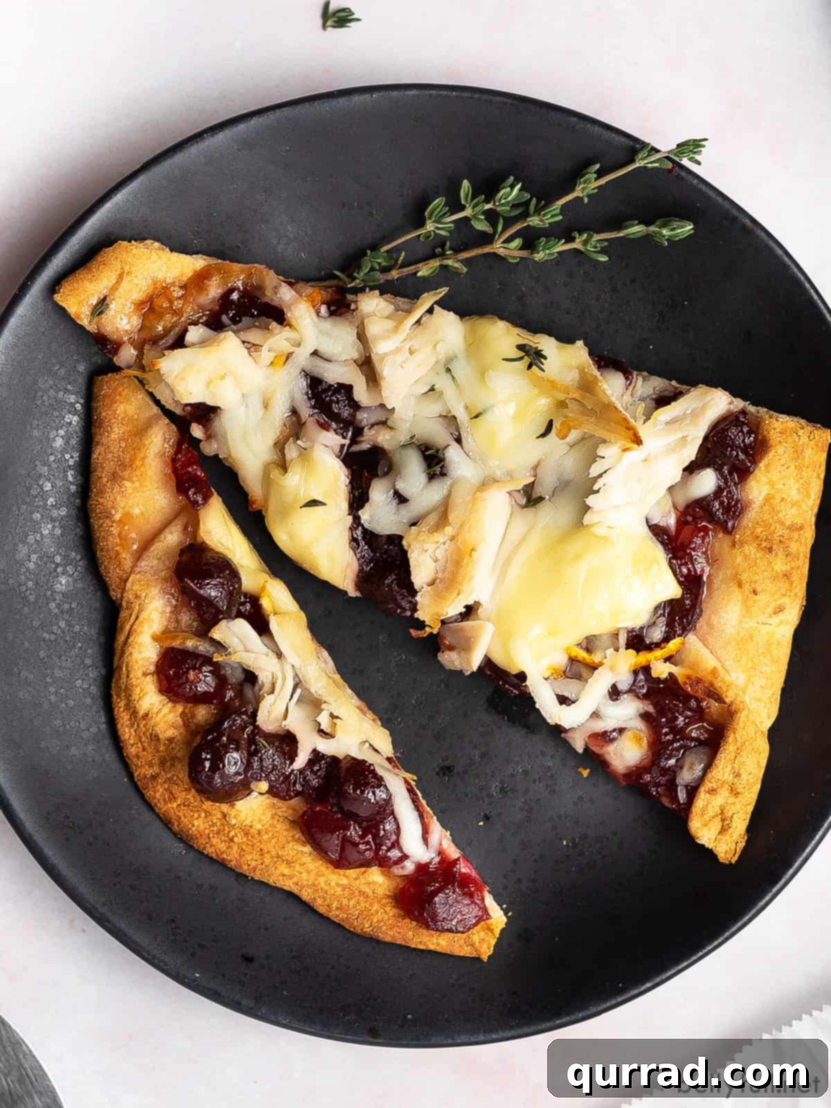 Two slices of Thanksgiving leftover pizza on a black plate, with visible turkey, cranberry, and brie